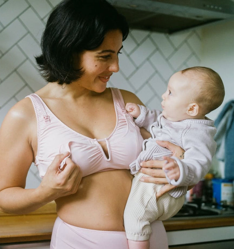 customer wearing Belle maternity bra in rosy, holding baby, opening the drop down cup