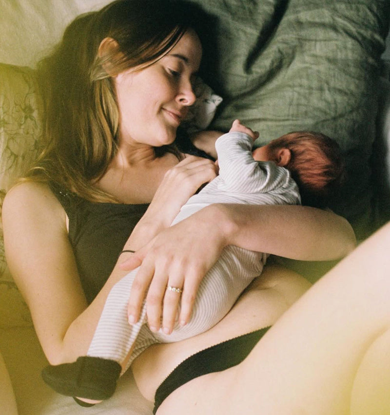 customer wearing Belle bra in shield black, lying down with baby, breastfeeding